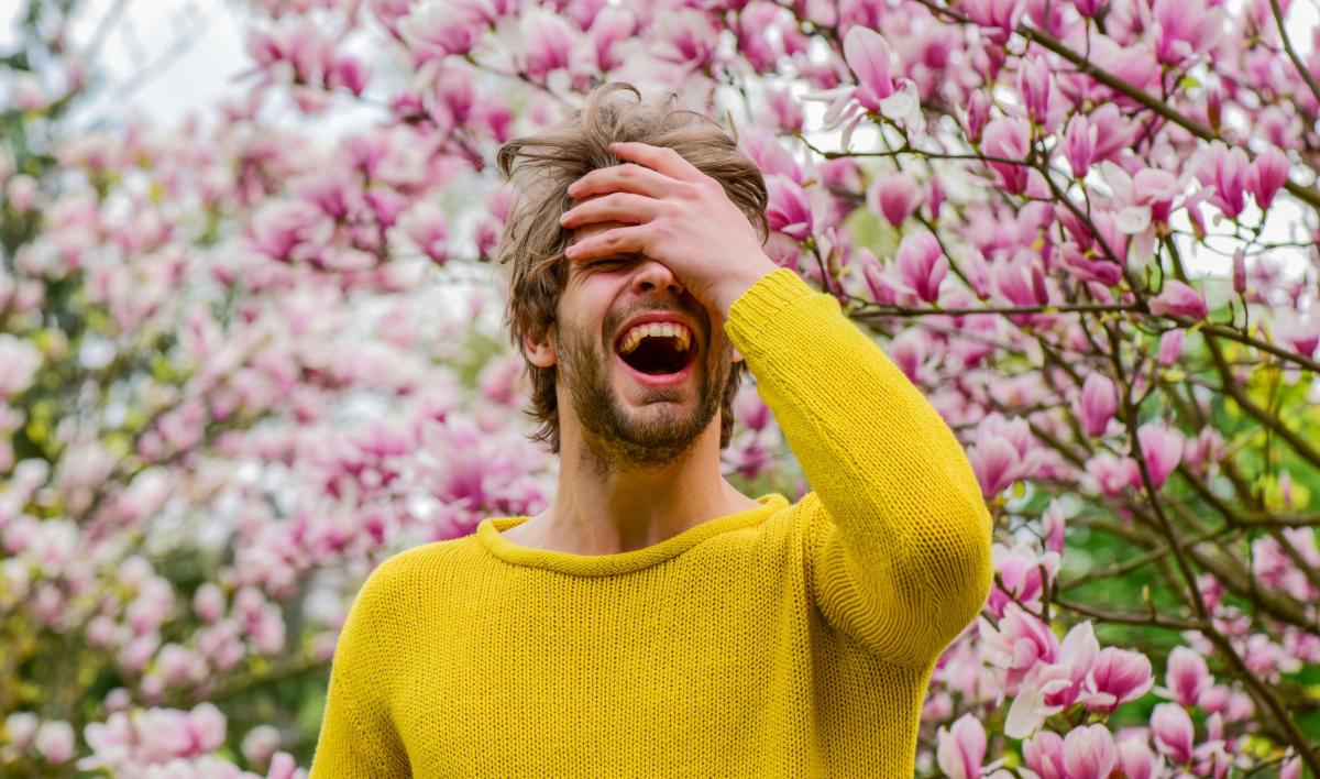een man met gele trui staat voor een magnolia en lacht uitbundig 