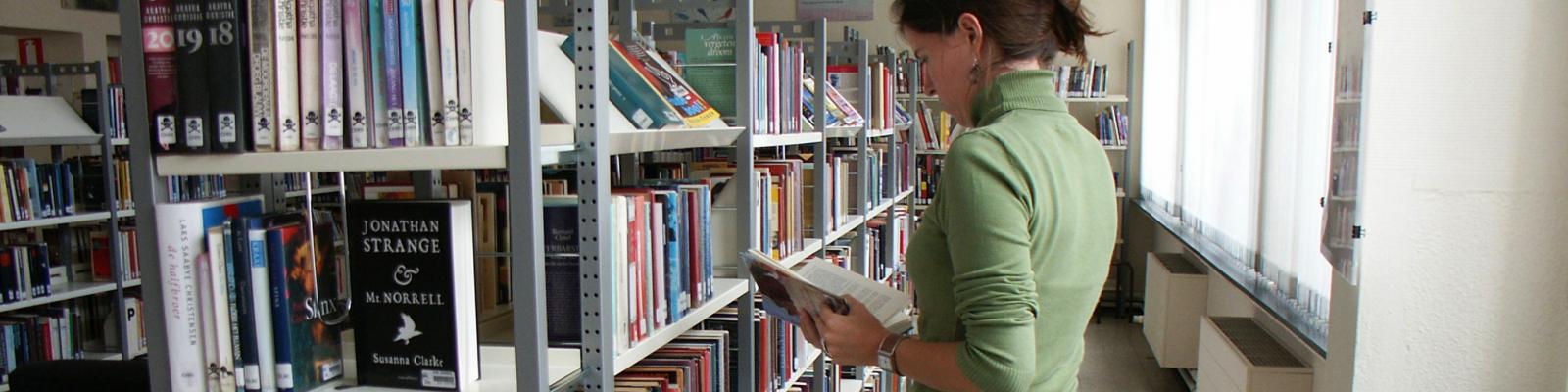 jonge vrouw die in de bibliotheek bladert in een boek