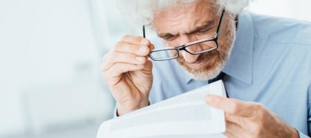 een man met grijs krulhaar probeert de kleine lettertjes op een document te lezen