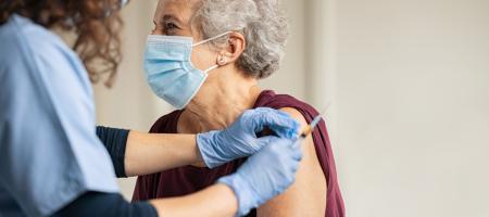 een oudere dame met een mondmasker krijgt een vaccin toegediend door een dokter