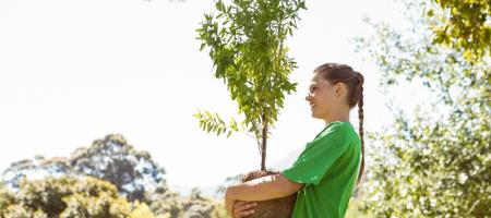 een jonge vrouw met een groen t-shirt loopt houdt een jonge boom vast