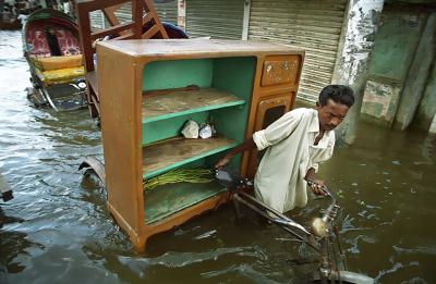 een inwoner van Bangladesh sleurt met zijn inboedel door een ondergelopen straat