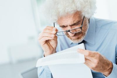 een man met grijs krulhaar probeert de kleine lettertjes op een document te lezen