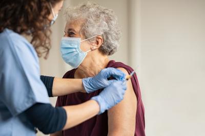 een oudere dame met een mondmasker krijgt een vaccin toegediend door een dokter