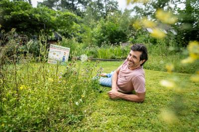 Dieter Coppens ligt op het gras met naast hem een stuk verwilderd gazon met een bermbordje in.