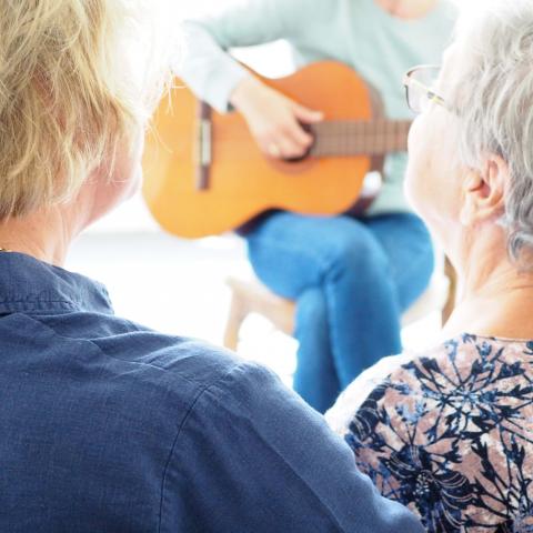 iemand speelt gitaar en mantelzorger en persoon met dementie zingen